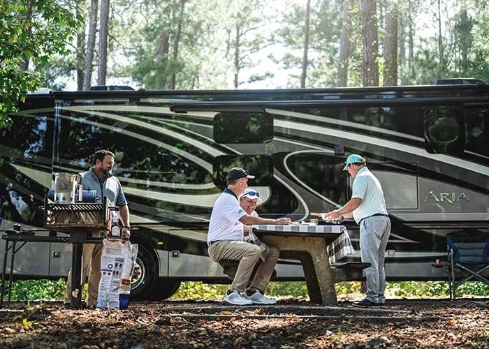2021 Thor Aria Class A Diesel Pusher RV Lifestyle side view men grilling and eating at campsite