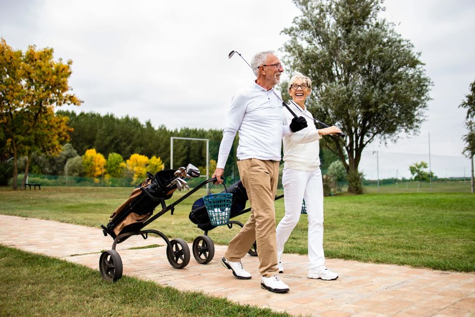 An elegant senior couple enjoying free time in retirement by playing golf and walking to the practice range.