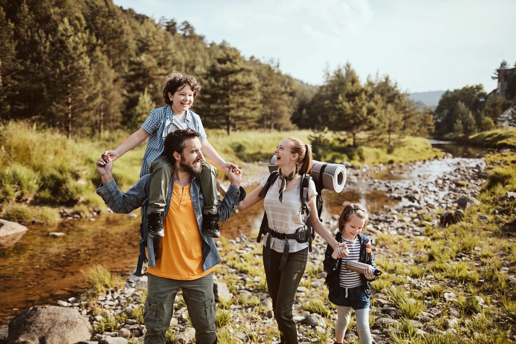 Young family crossing a creek while hiking in the forest and mountains